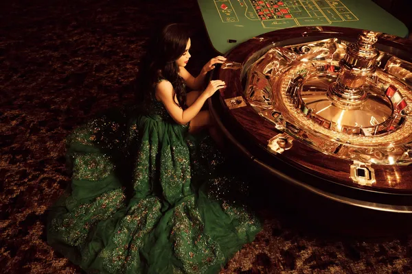 A woman in a luxurious green gown next to an ornate roulette wheel, capturing the upscale casino mood of L85.